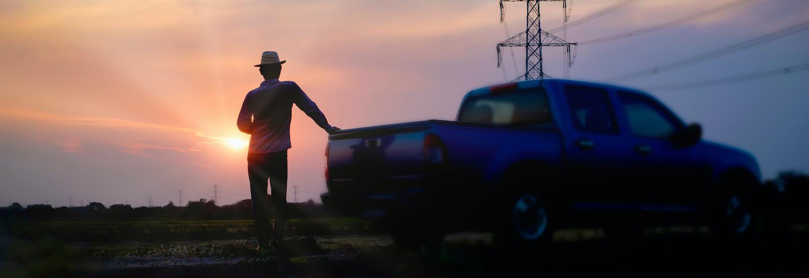 一名男子站在皮卡车后面看日落，背景是电力线