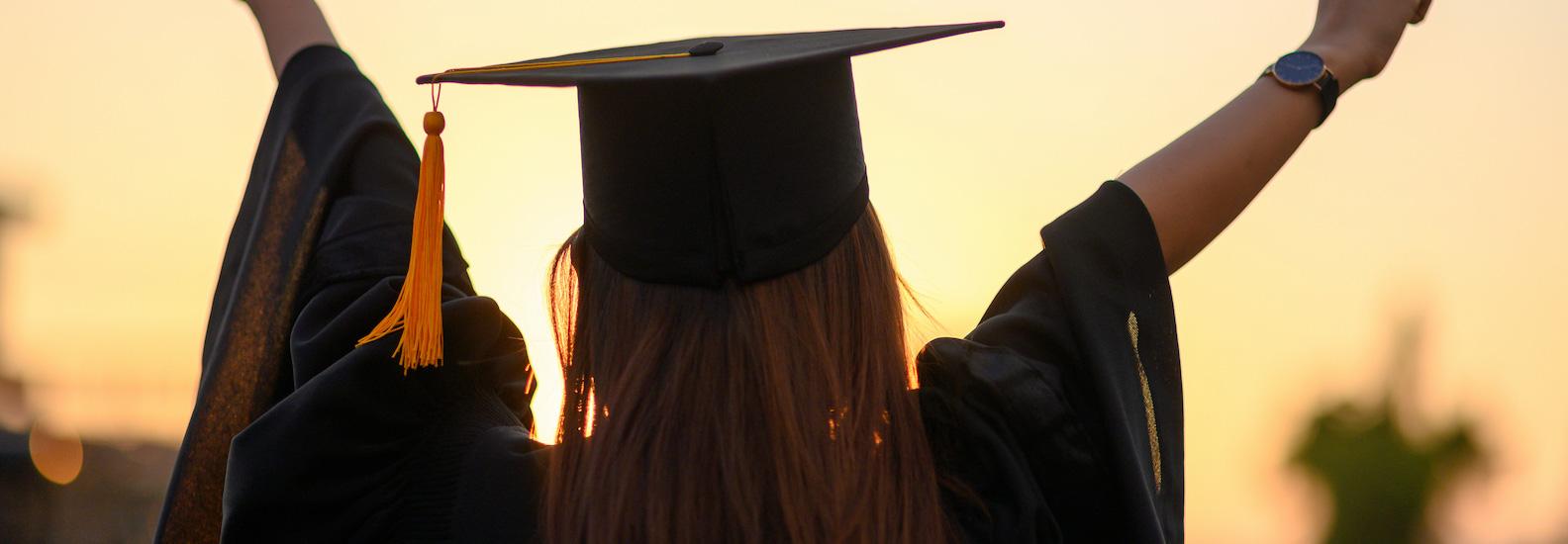 一名女子戴着黑色的毕业帽，身穿长袍，高举双臂庆祝